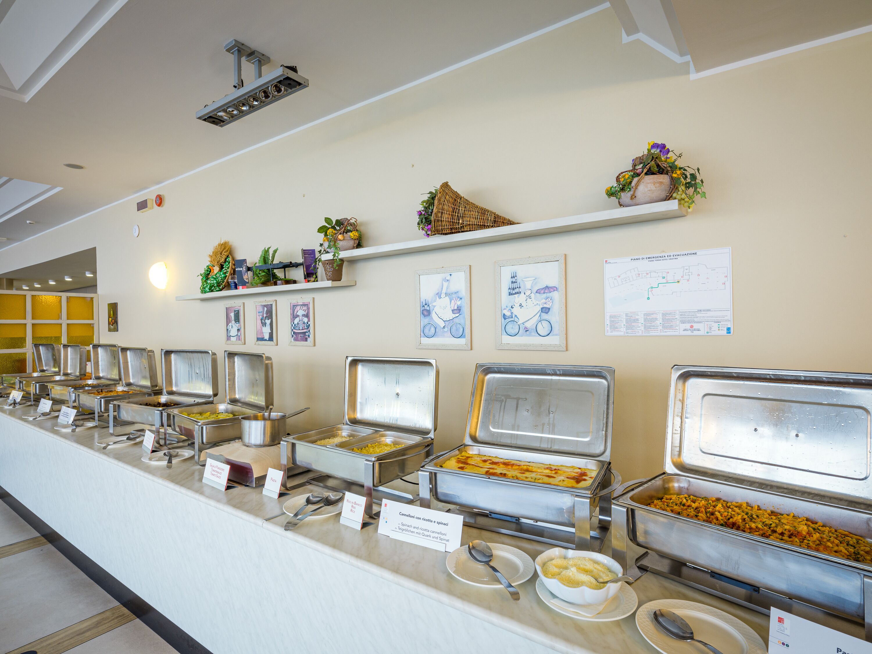 Un banco buffet con diverse postazioni gastronomiche, tra cui pasta, insalate e un sformato.