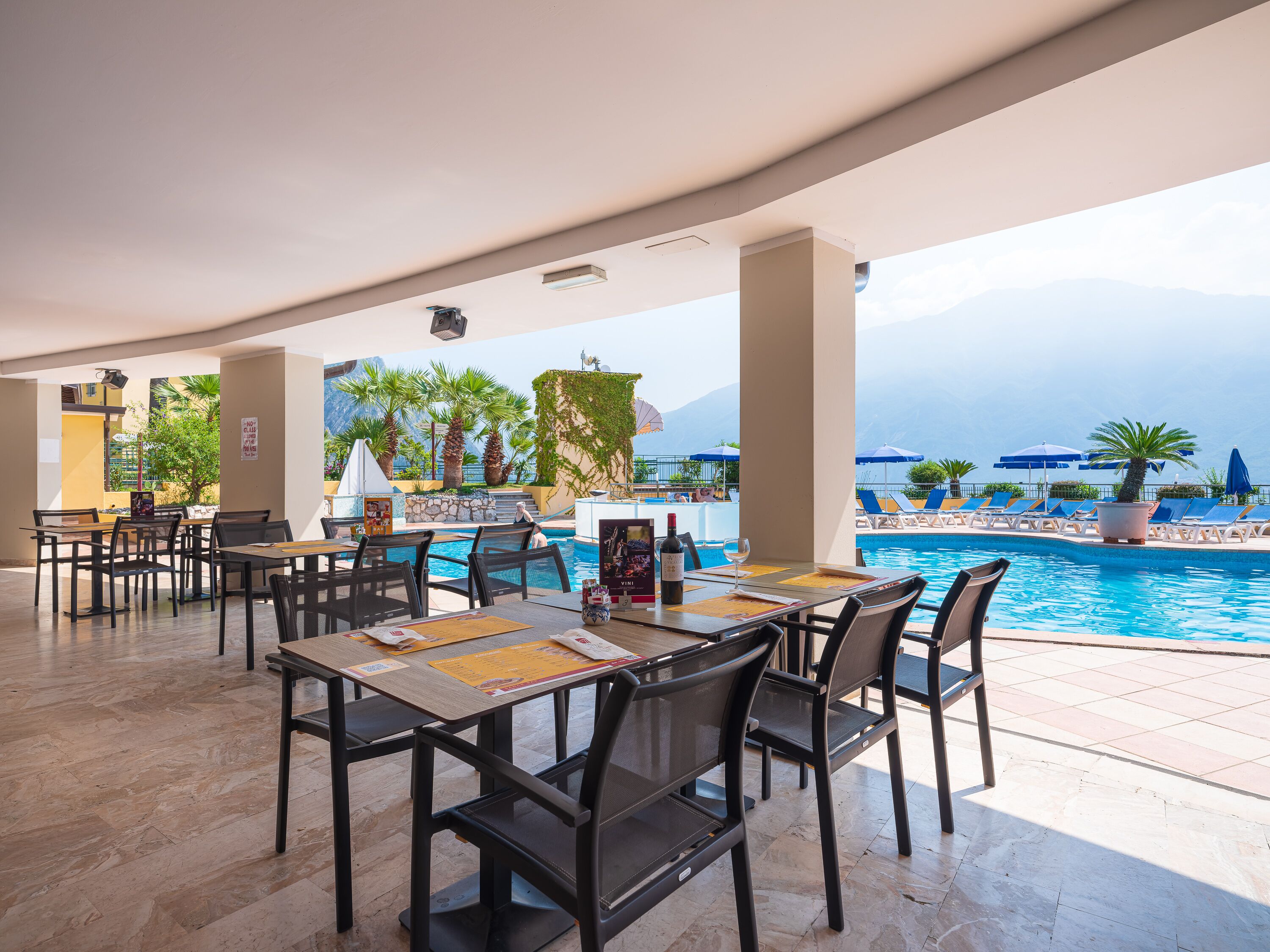 Un restaurante junto a la piscina con mesas al aire libre, piscina y vistas a montañas.