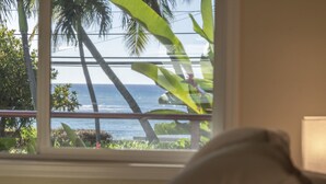 A room with a view of the ocean and palm trees through a window. - Maui Beach House (Lahaina)
