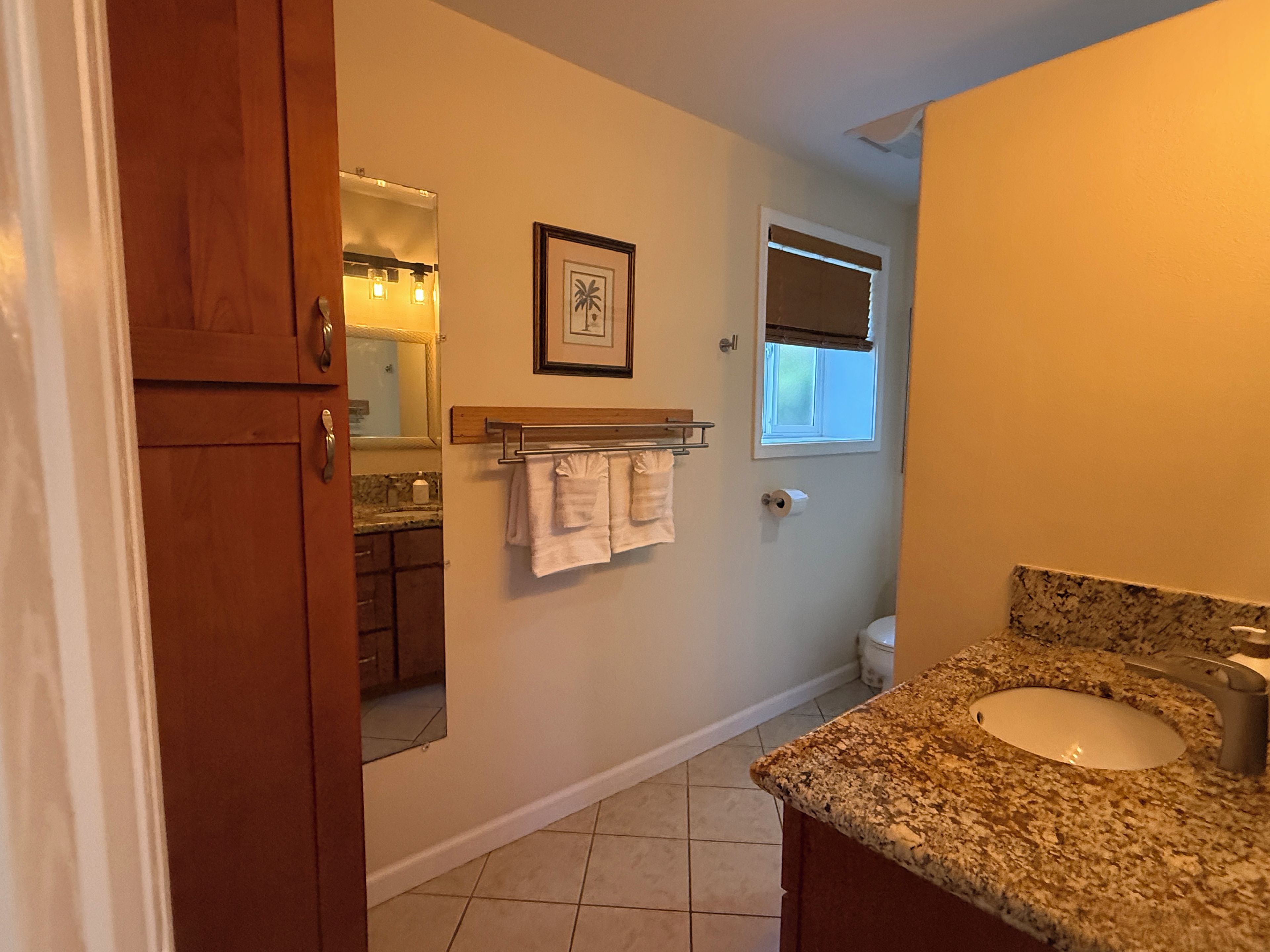 A bathroom with a sink, mirror, towel rack, and a window with blinds.