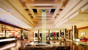 Een moderne lobby met een centraal waterkunstwerk, marmeren vloeren en een receptiebalie.