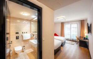 Een moderne hotelkamer met een glazen deur naar een badkamer, een bed met een rode hoofdbord, een televisie en een bureau met een stoel.