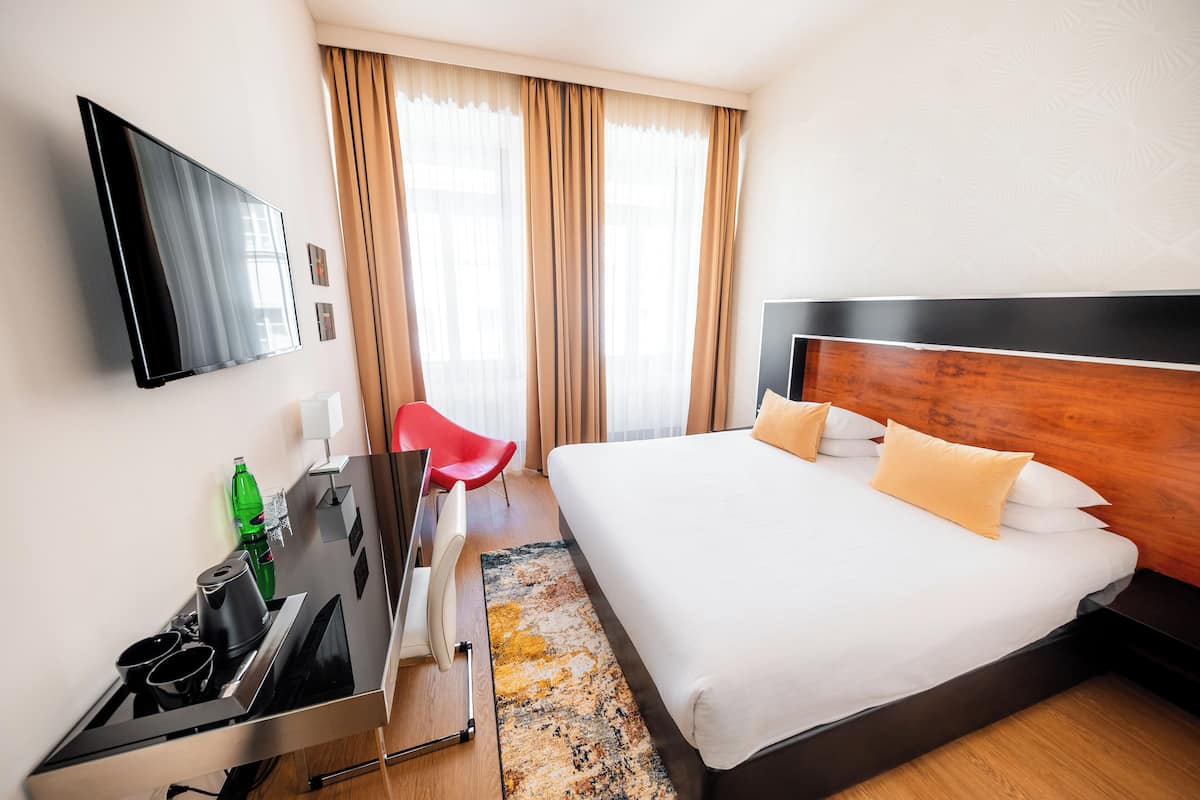 Une chambre d’hôtel avec un lit, une télévision, un bureau avec une chaise et une fenêtre avec des rideaux.
