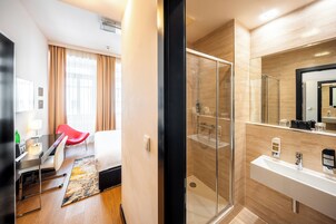 Um banheiro de hotel moderno com box de vidro, pia branca e espelho grande.