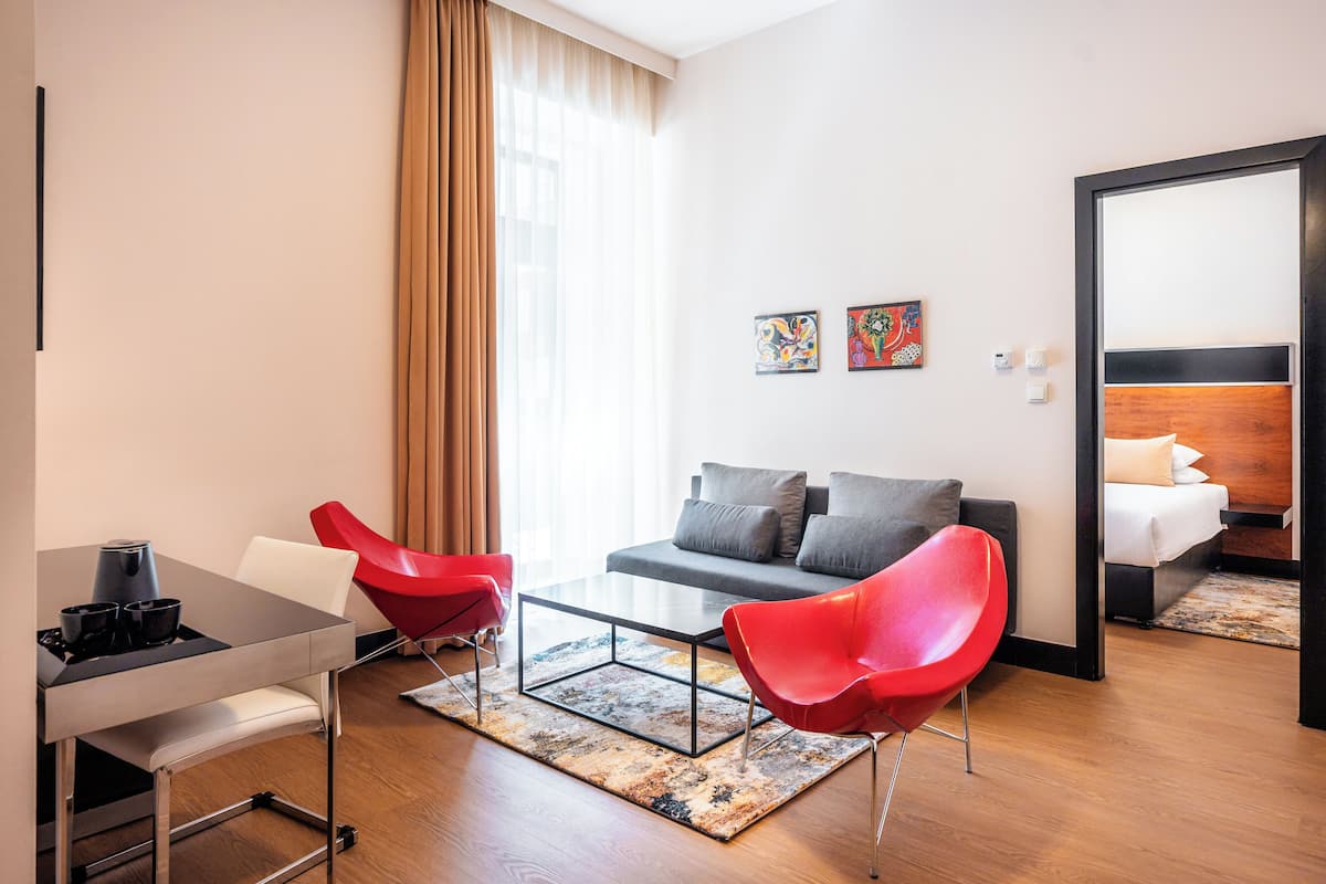 Une chambre d’hôtel moderne avec un canapé, deux fauteuils rouges, une petite table et un lit doté d’une tête de lit.