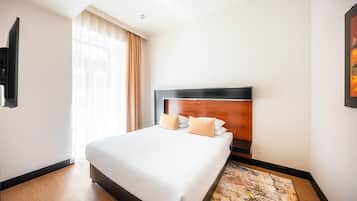 A hotel room with a large bed, a wooden headboard, a window with curtains, and a painting on the wall.