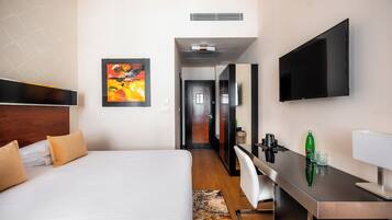 A hotel room with a bed, a desk, a chair, a TV, and a painting on the wall.