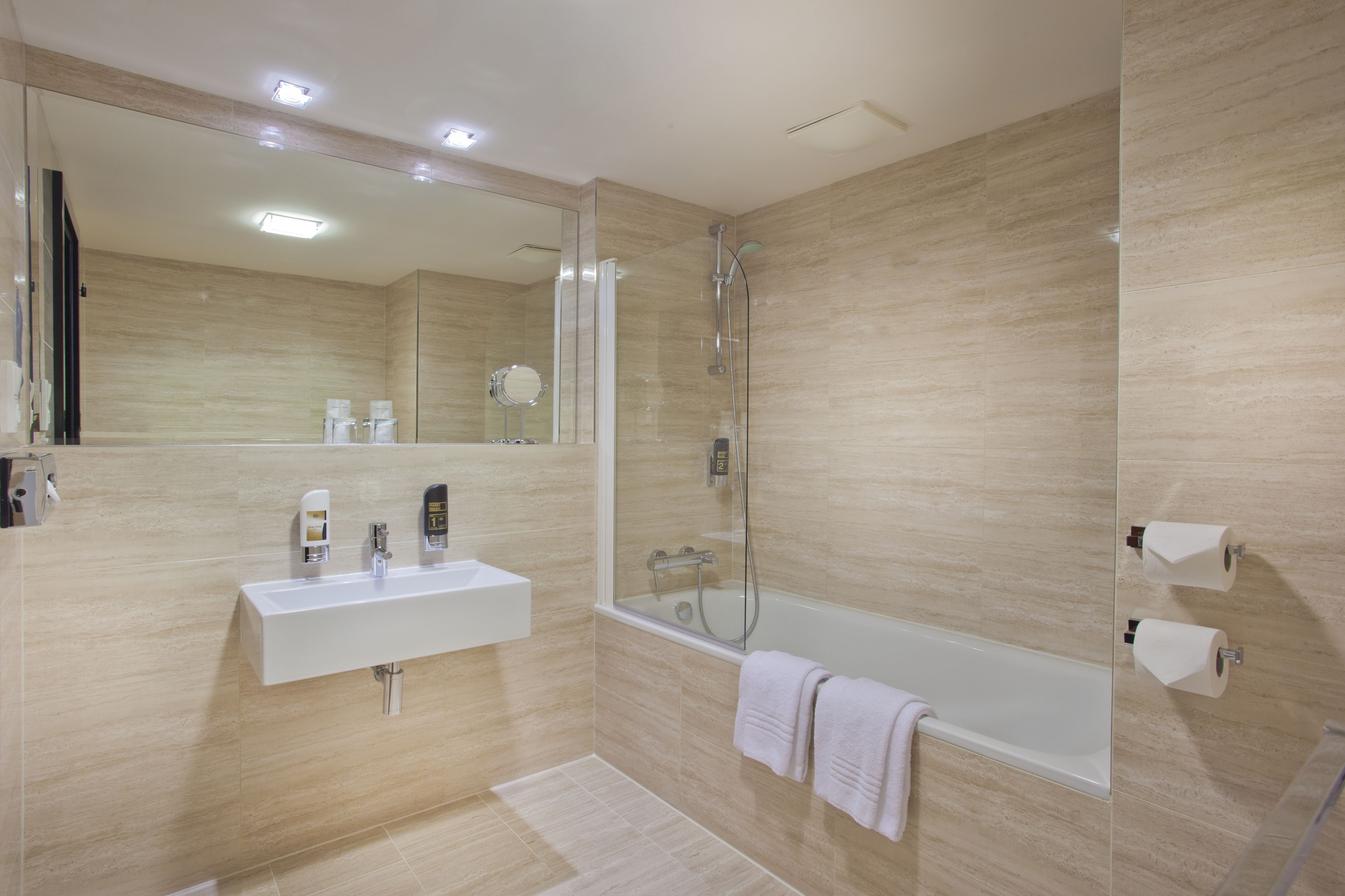 A modern bathroom with a large mirror, a white sink, a bathtub, and a shower.