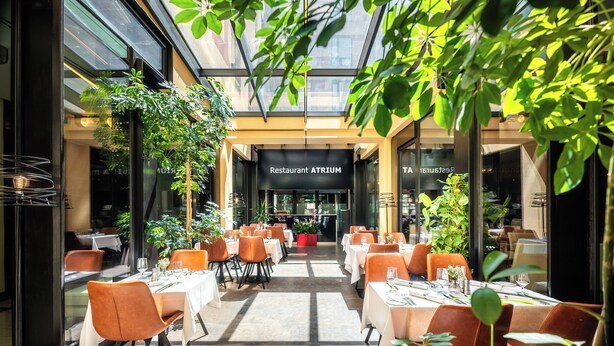 En restaurang med en innergård med bord och stolar, krukväxter och ett glastak.