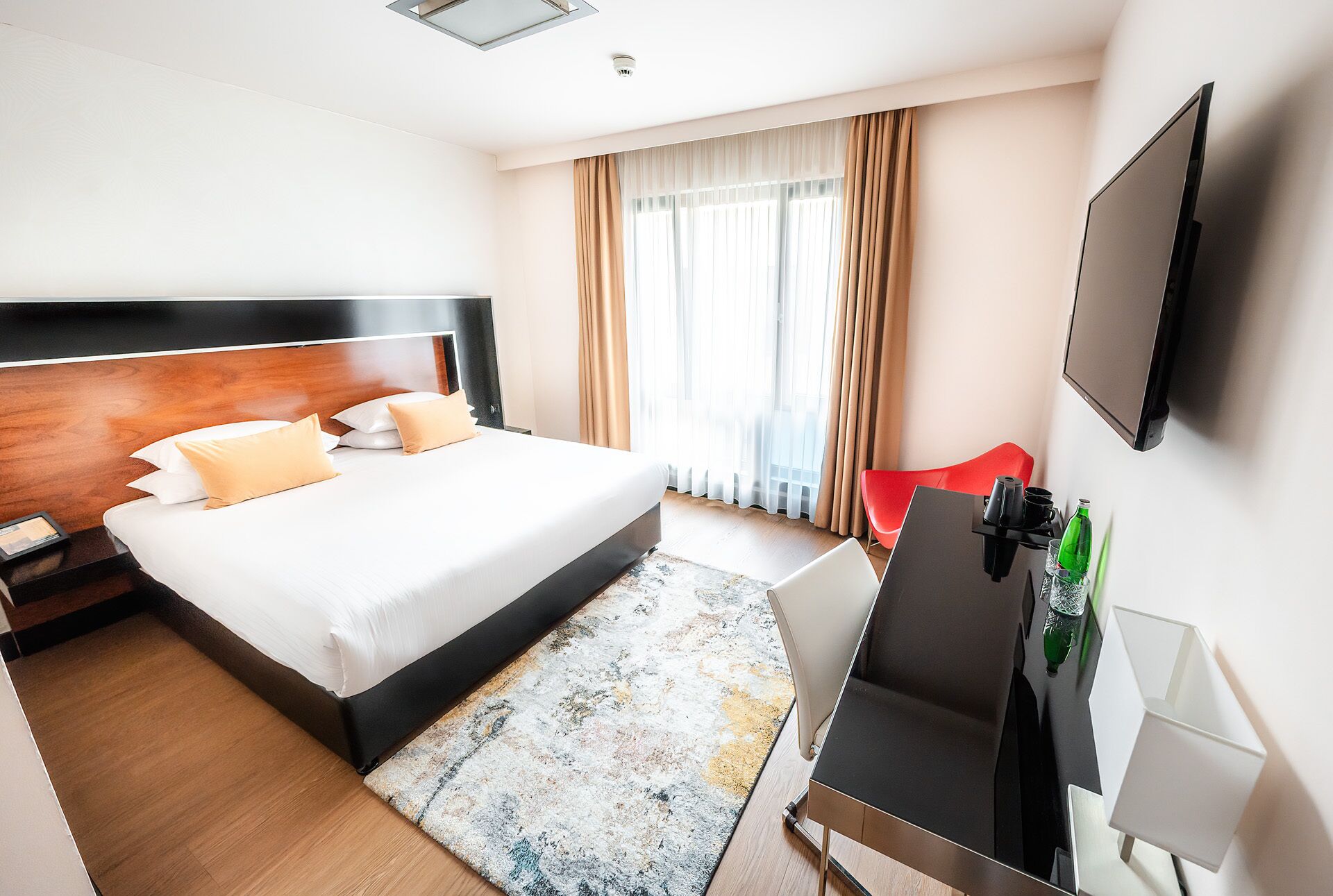 Habitación de hotel con una cama grande, un escritorio con silla, televisor y ventana con cortinas.