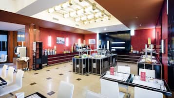 Un comedor moderno de hotel con varias estaciones de buffet, sillas blancas y un interior limpio y bien iluminado.