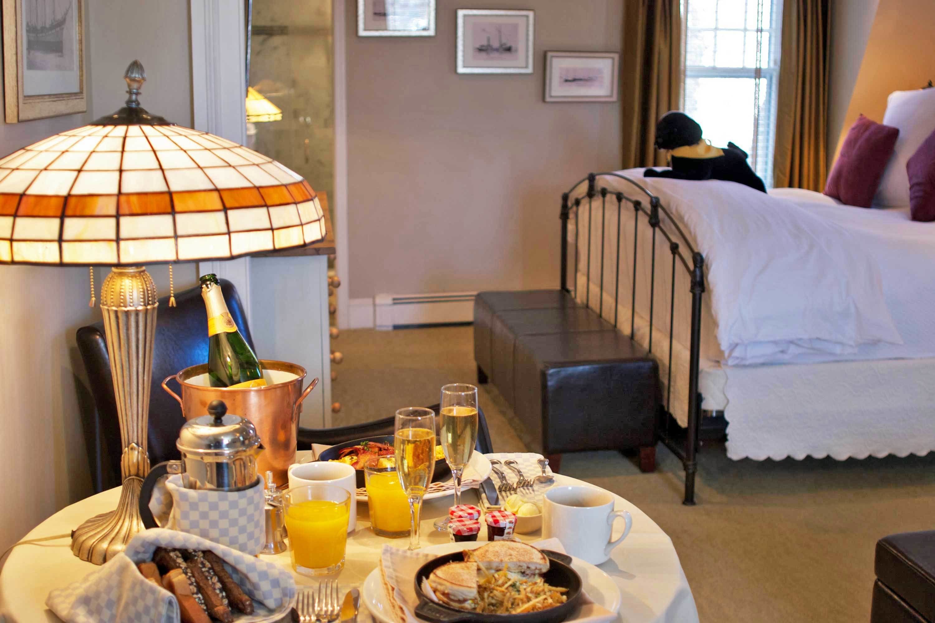 Un desayuno con una mesa, una lámpara, una botella de champán y una cama al fondo.