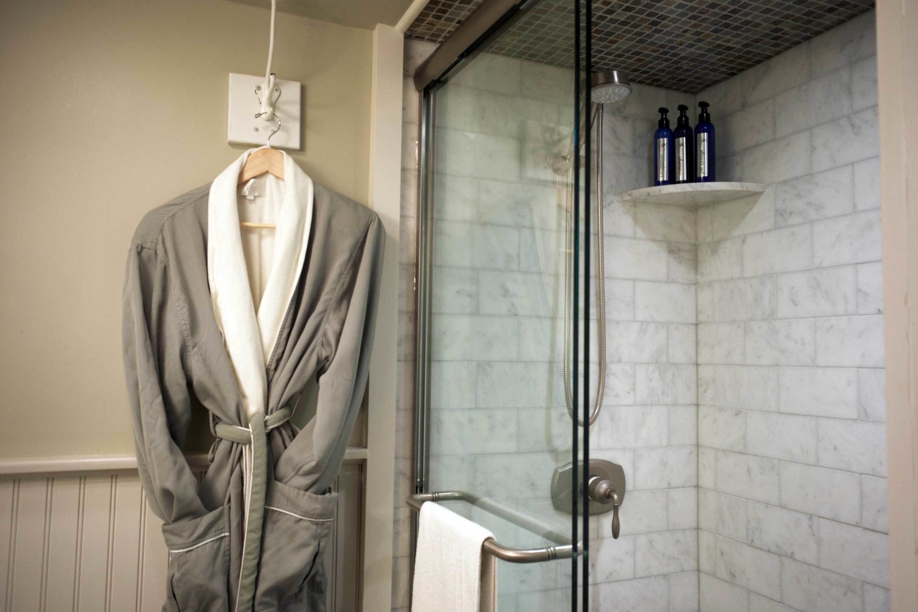 Une salle de bain avec une douche à parois de verre, un porte-serviettes avec un peignoir, et une étagère avec des bouteilles.