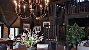 A dining area with a chandelier, a large table, chairs, and a vase with flowers. - Mill House Inn (East Hampton)