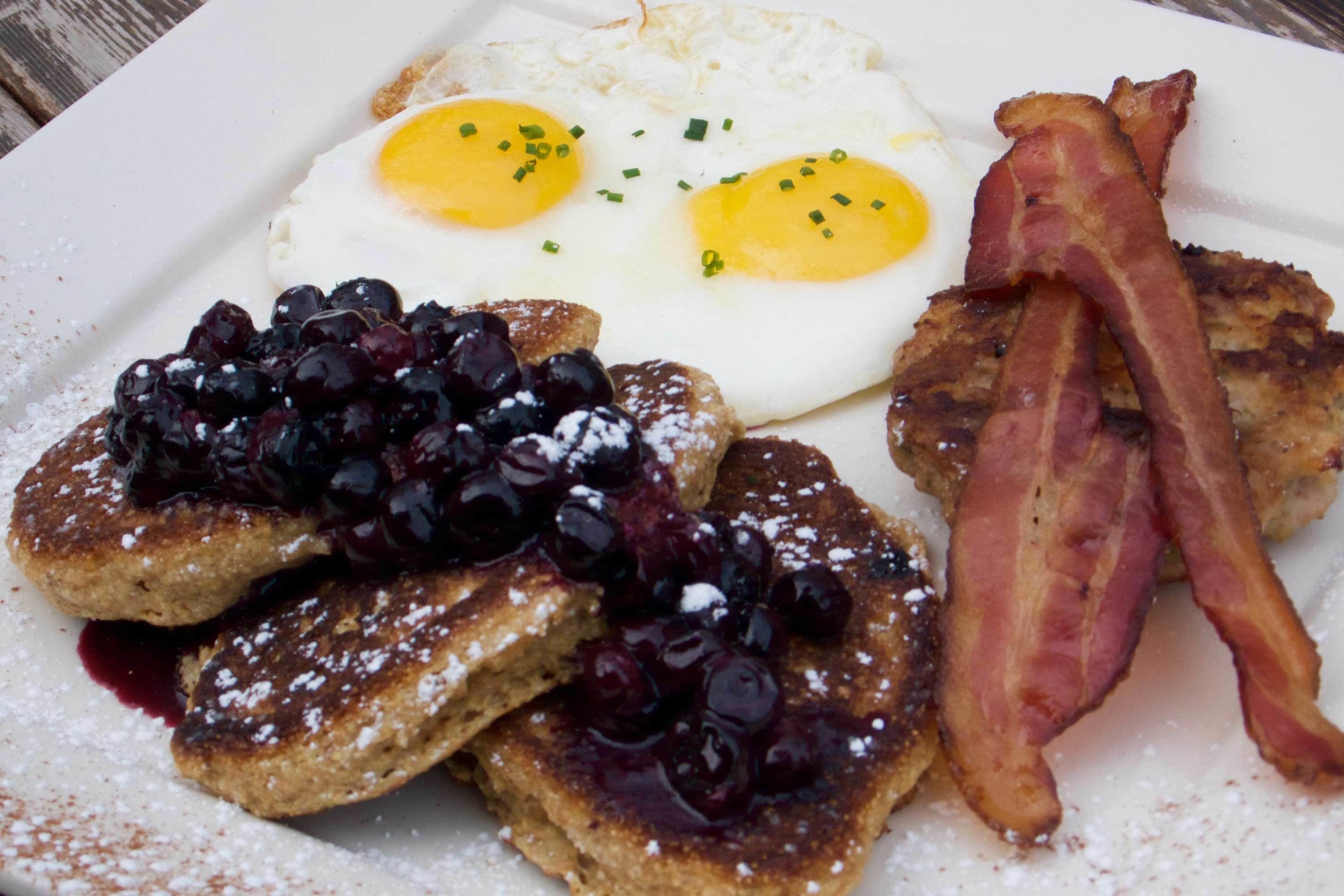 A plate with French toast, two fried eggs, and bacon.