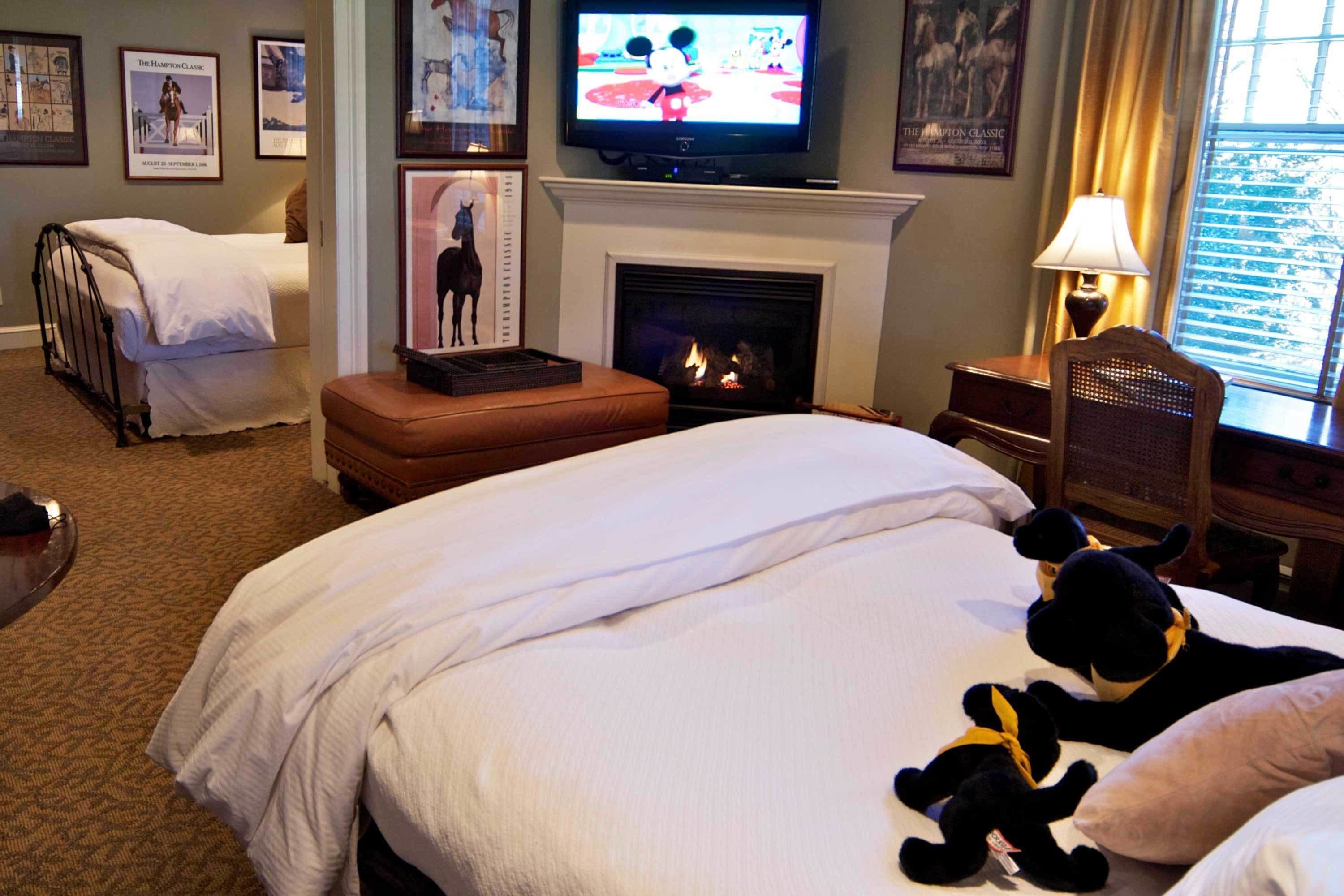 A hotel room with a large bed, a television, a fireplace, and a window with curtains.