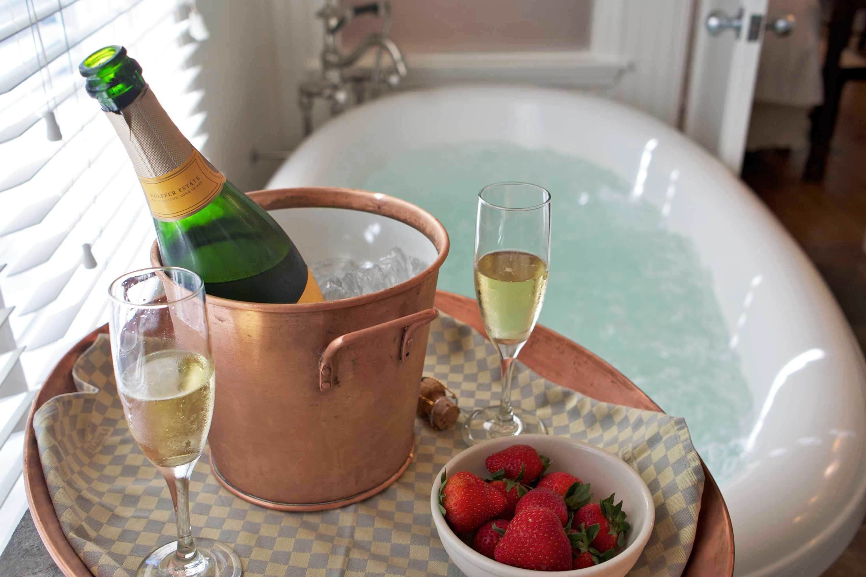 Ein Kupferkübel mit einer Champagnerflasche, zwei Champagnergläsern, einer Schale Erdbeeren und einer Badewanne.