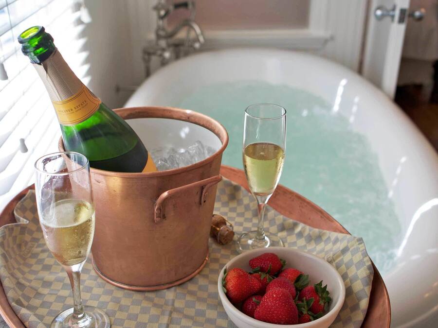 Ein Kupferkübel mit einer Champagnerflasche, zwei Champagnergläsern, einer Schale Erdbeeren und einer Badewanne.