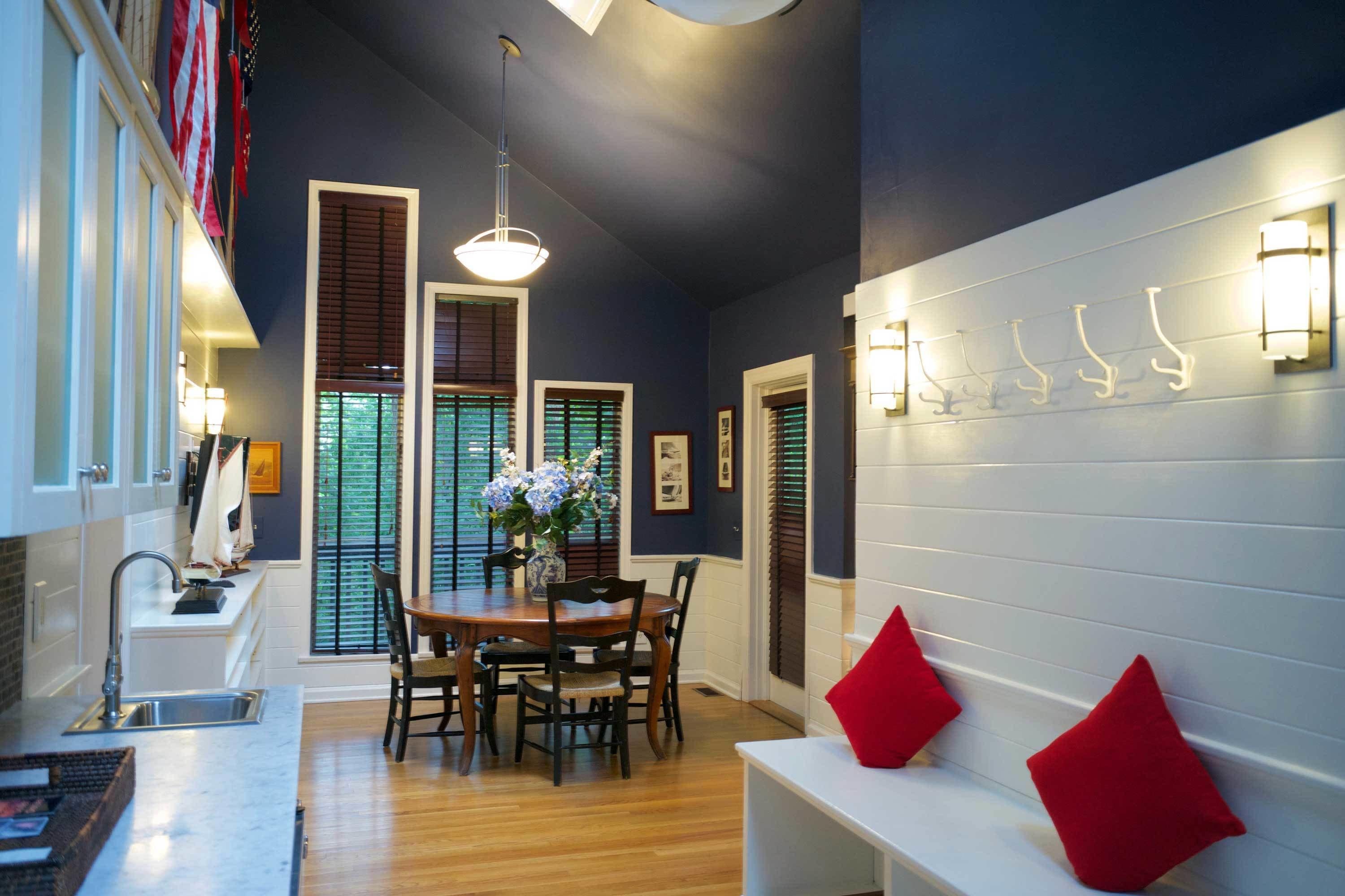 A modern kitchen with a wooden dining table, chairs, and a white bench with red cushions.
