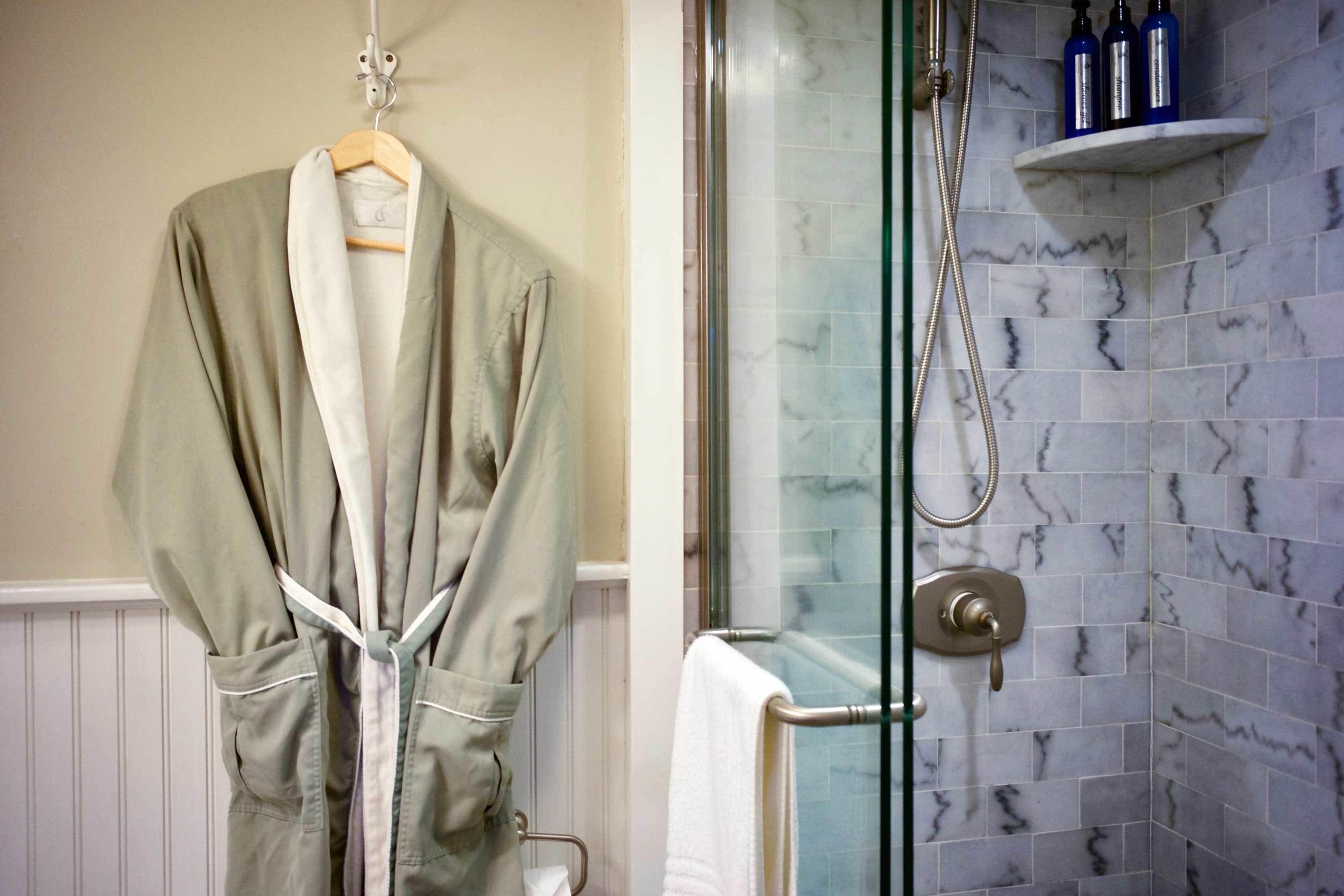A bathroom with a glass shower enclosure, marble tiles, and a robe hanging on a rack.