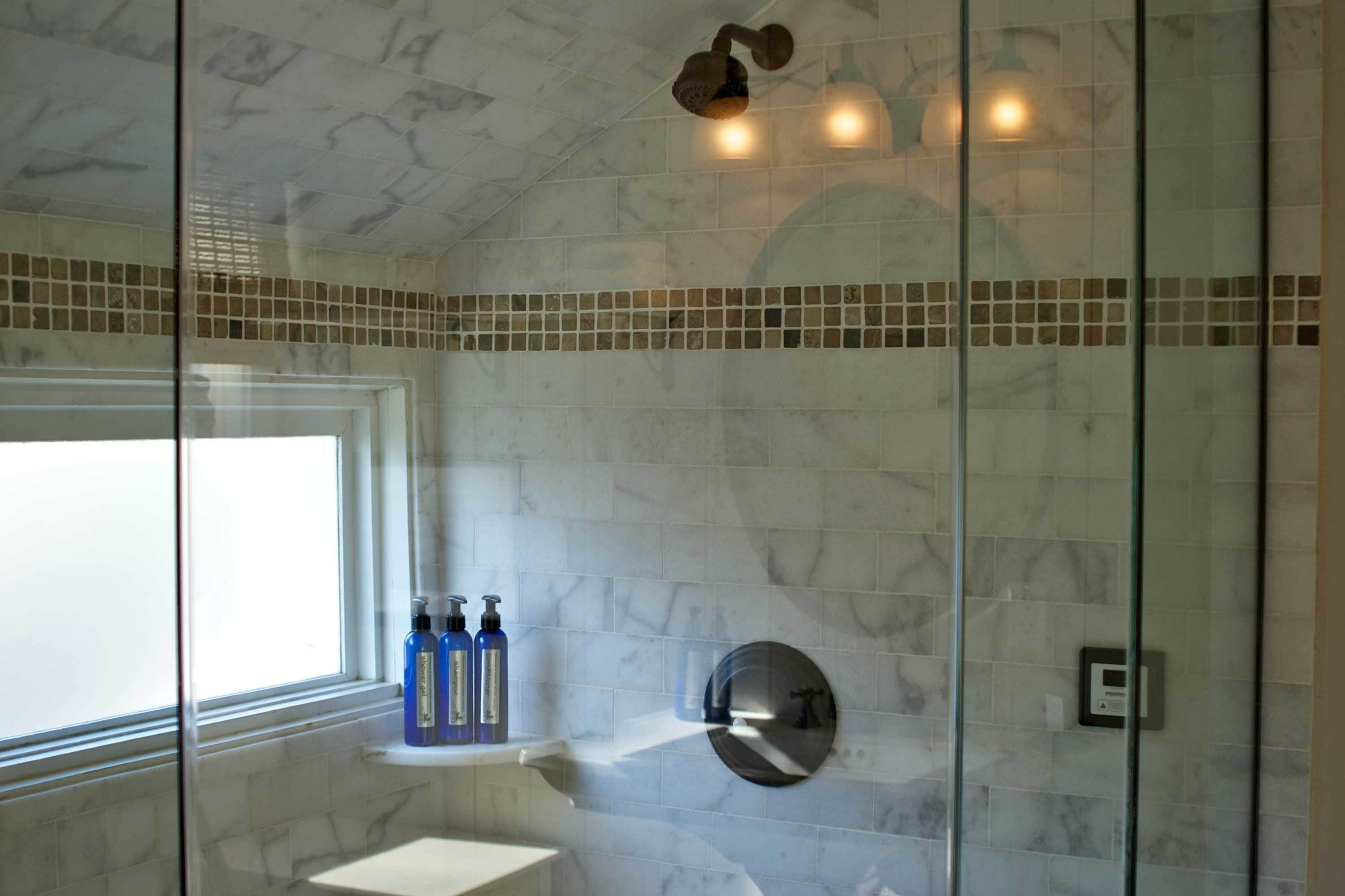 Un baño con cabina de ducha de vidrio, pared con azulejos de mármol y una ventana.