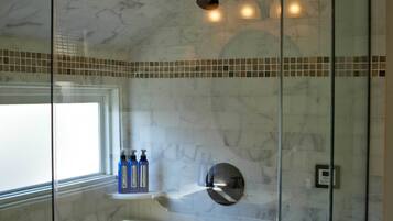 Un baño con cabina de ducha de vidrio, pared con azulejos de mármol y una ventana.