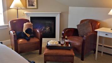 A hotel room with two leather armchairs, a small ottoman, a tray with snacks and drinks, a fireplace, and a desk with a lamp.