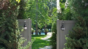 A wooden gate leading to a pathway surrounded by lush greenery and trees. - Mill House Inn (East Hampton)