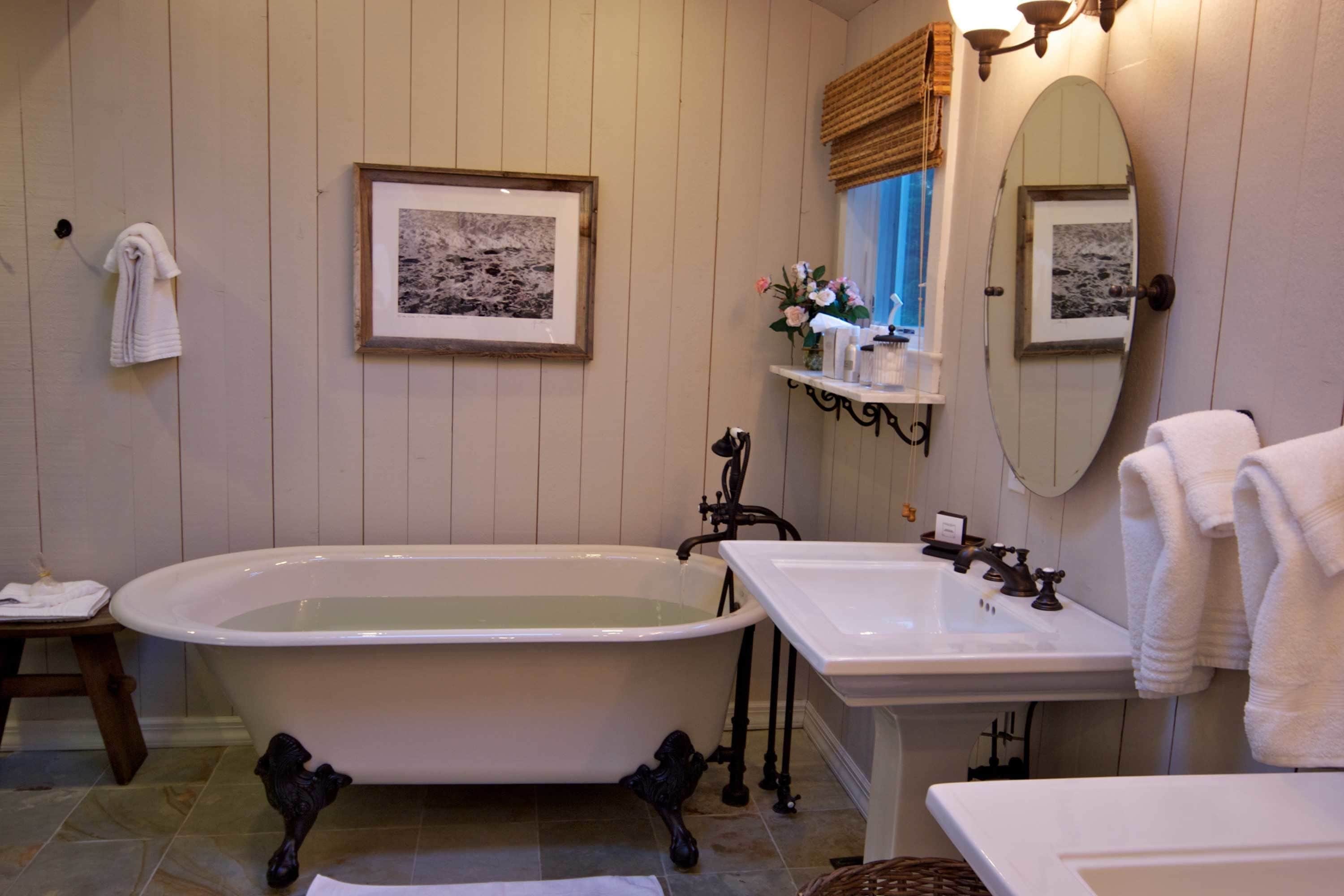 Ein Badezimmer mit einer Badewanne auf Pfoten, einem weißen Waschbecken und einem Spiegel mit Bilderrahmen.