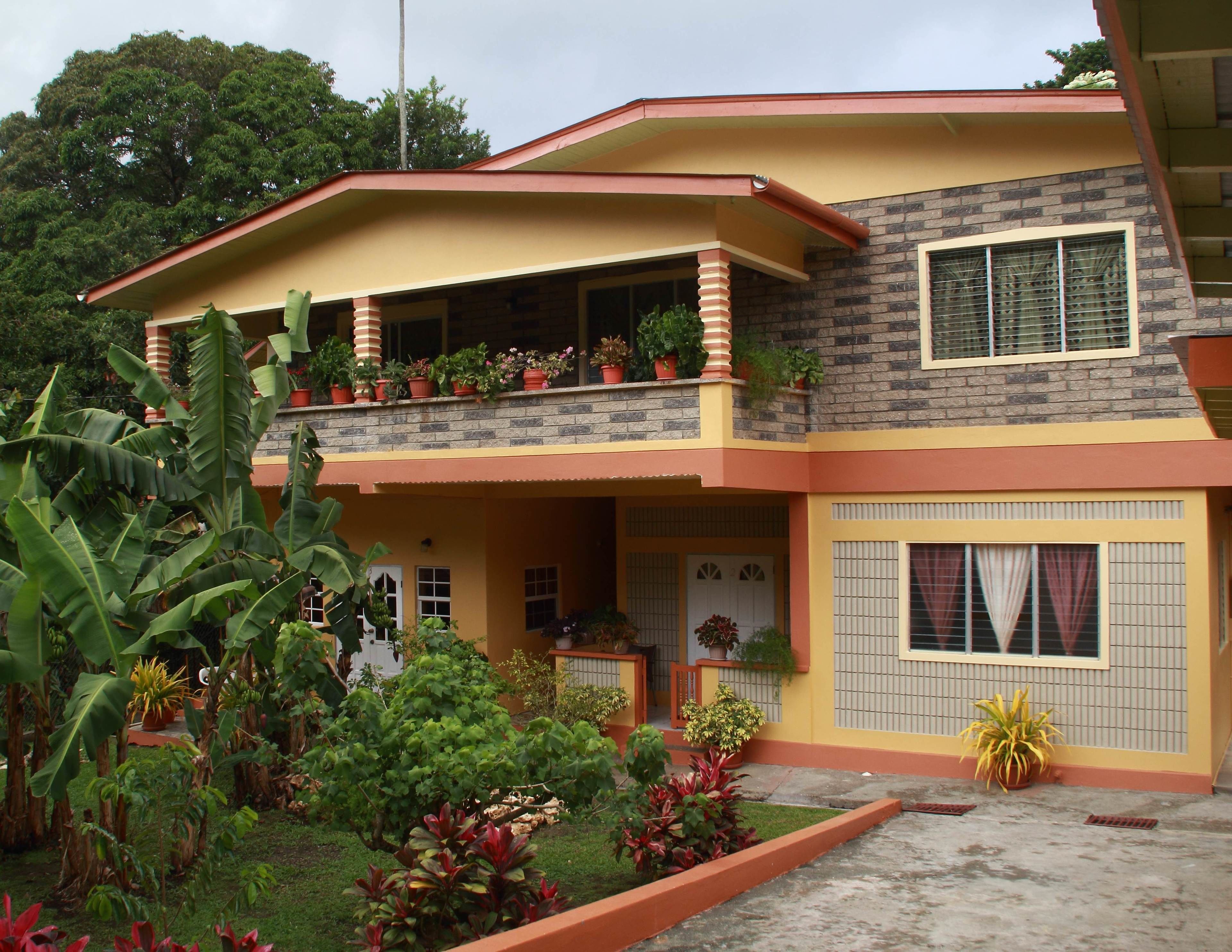 A two-story house with a balcony, surrounded by lush greenery and potted plants.