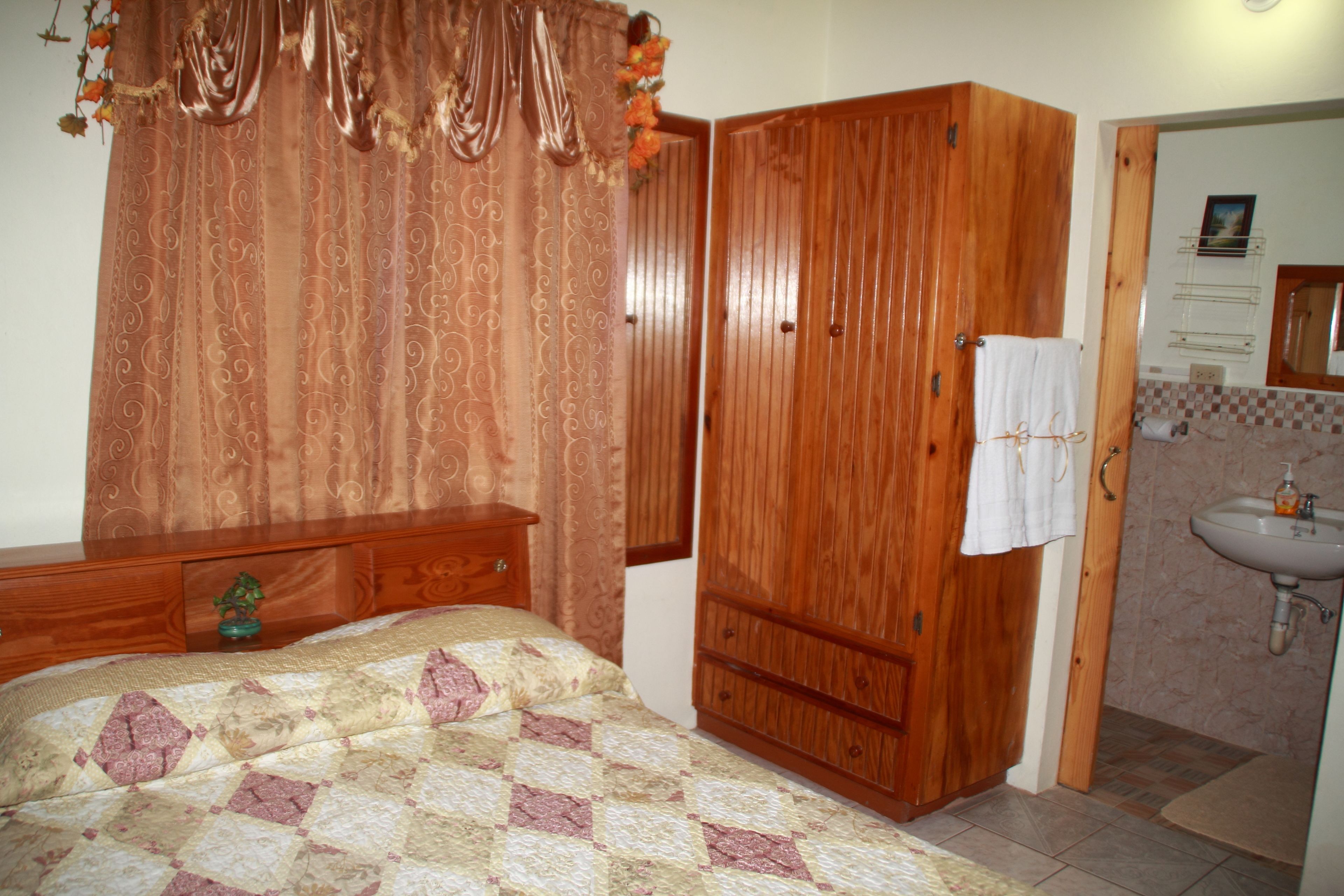 A bedroom with a bed, wooden wardrobe, and a bathroom with a sink and mirror.