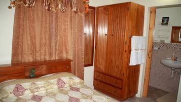A bedroom with a bed, wooden wardrobe, and a bathroom with a sink and mirror.