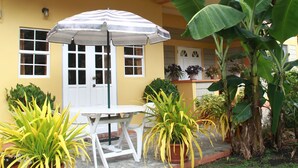 A yellow building with a white door, windows, and a covered patio area with a table and chairs. - Greenhaven Cottage B&B (Les Coteaux)