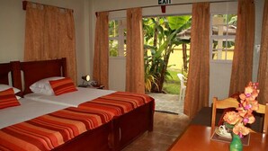 A hotel room with a large bed, a small table with a vase of flowers, and a view of the garden through the window. - Greenhaven Cottage B&B (Les Coteaux)