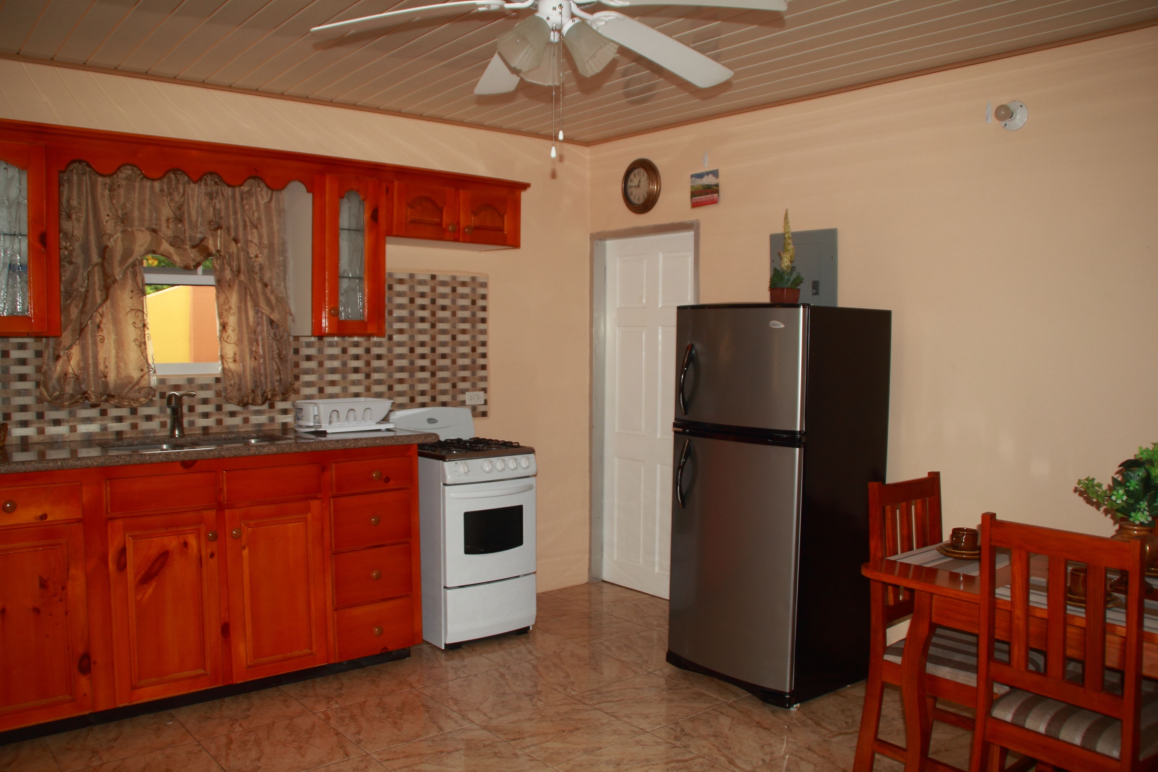A kitchen with wooden cabinets, a stove, a refrigerator, and a dining table with chairs.