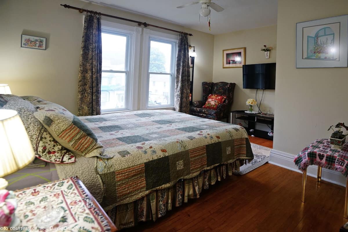 A bedroom with a large bed, a chair, a TV, and a desk.