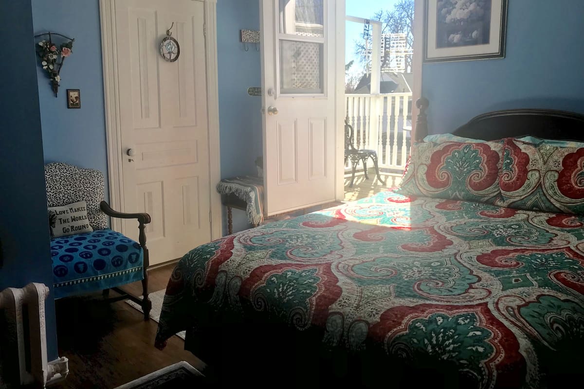 A bedroom with a bed, a chair, a door, and a view of the outside.