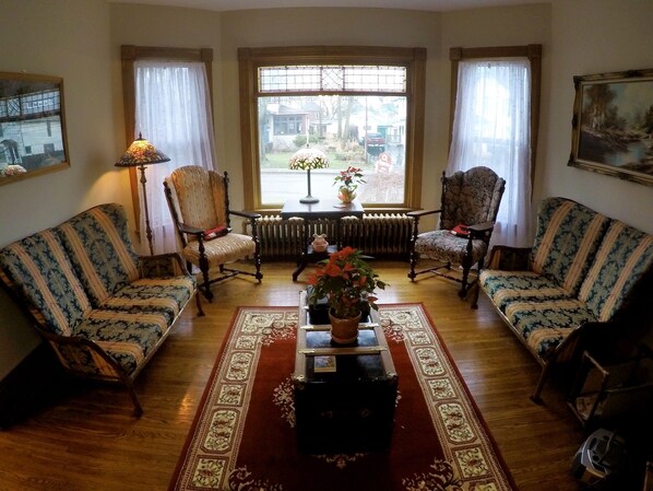 A traditional living room with two patterned sofas, a coffee table with a vase, and a view through a large window.