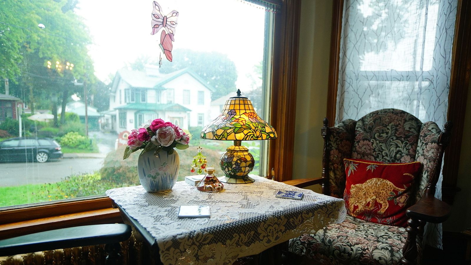 A room with a table set for tea, a vase with flowers, a lamp, and a chair with a leopard pillow.