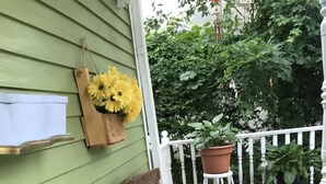 A wooden bench with a striped cushion, a hanging planter with yellow flowers, and a potted plant on a wooden deck with a white railing. - Niagara Inn Bed & Breakfast (Niagara Falls)