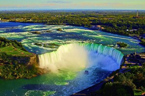 A large waterfall with a boat ride in the foreground, surrounded by lush greenery and a distant cityscape. - Niagara Inn Bed & Breakfast (Niagara Falls)