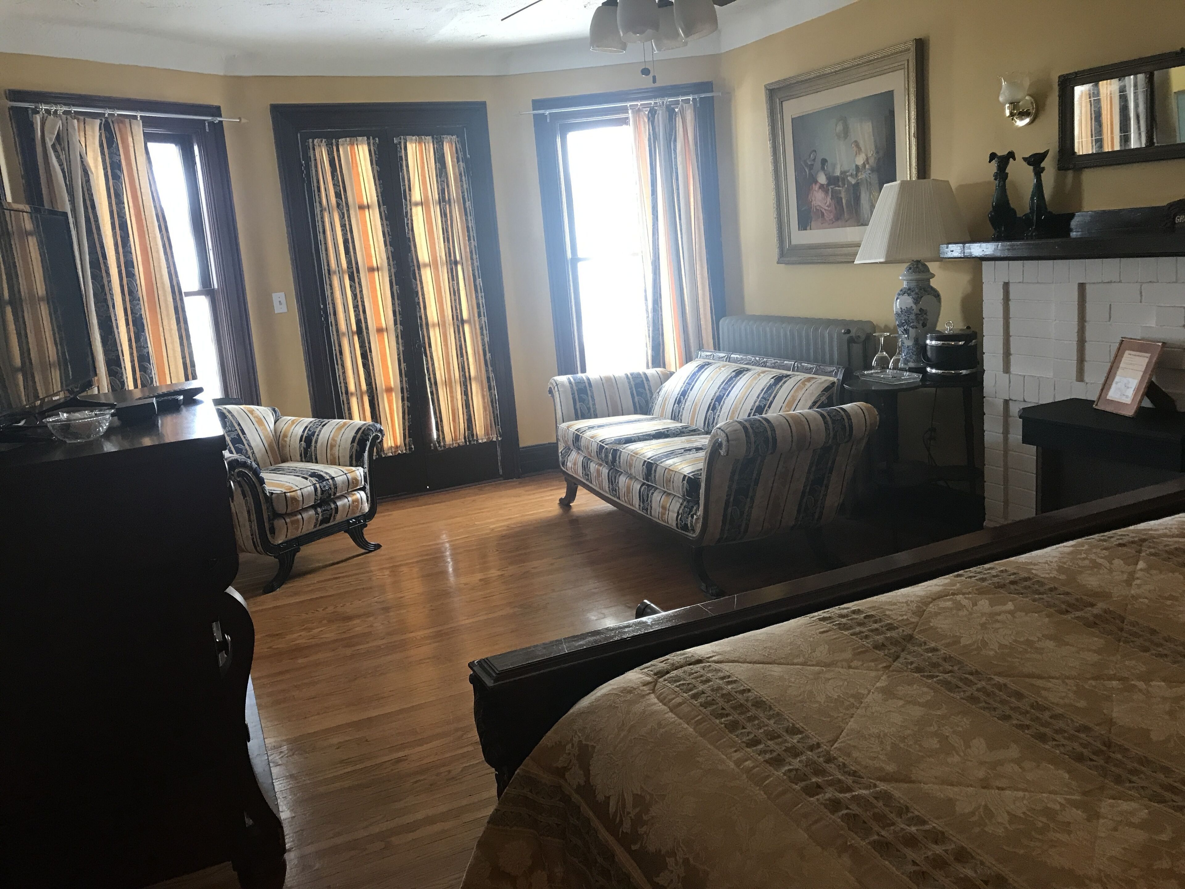 A hotel room with two sofas, a bed, a fireplace, and a painting on the wall.