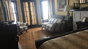 A hotel room with two sofas, a bed, a fireplace, and a painting on the wall.