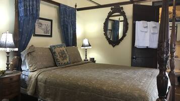 A four-poster bed with a canopy, a wooden headboard, and a large ornate mirror on the wall.