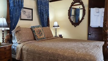 A bedroom with a bed, two bedside tables with lamps, a mirror, a framed picture, and a door with a towel hanging on it.