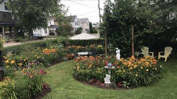 En velholdt have med mange blomster og en statue, omgivet af græsplæne og et par Adirondack-stole.