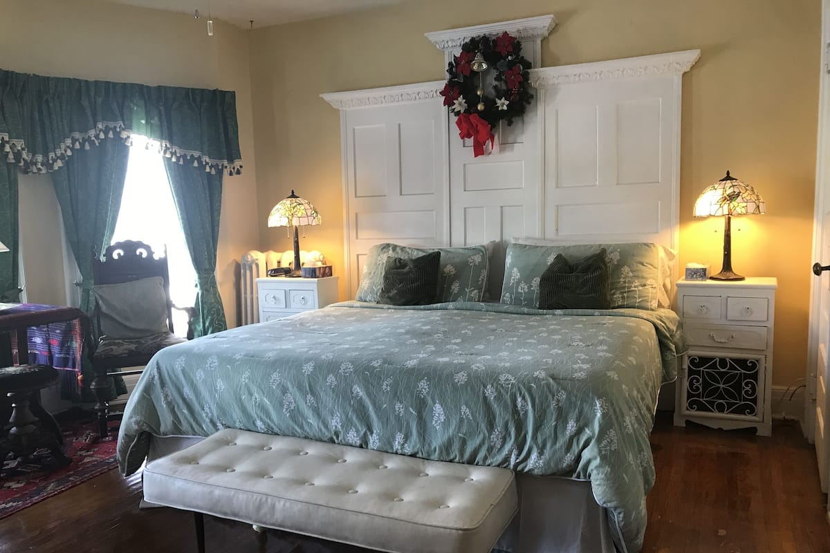 A bedroom with a bed, two bedside tables, a bench, a dresser, and a window with curtains.
