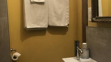 A bathroom with a yellow wall, a white sink, and two white towels hanging on the wall.
