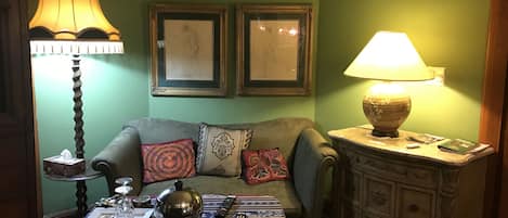A cozy living room with a sofa, two framed artworks, a lamp, a table with a teapot, and a cabinet.