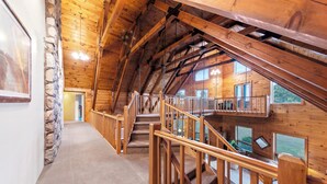 A wooden interior with a staircase leading to an upper level, stone wall on the left, and large windows on the right.